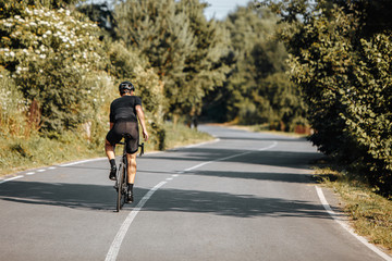 Back view of male athlete in sport clothing and protective helmet riding bike during sunny days. Active sportsman regularly training on fresh air.