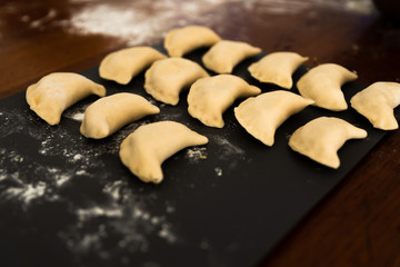 Uncooked russian vareniki on cutting wooden board with flour on baking paper. Process of making vareniki. top view.Typical Eastern European food, called dumplings, dumplings, dumplings, pies or pies