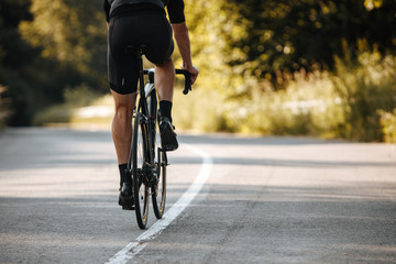 Fototapeta na wymiar Back view of cyclist in activewear riding professional bike on paved road with blur background of green plants. Concept of active lifestyle and hard training