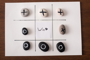 top view of tic tac toe game on white paper with pebbles marked with naught and cross, and win...