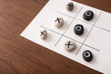 tic tac toe game on white paper with pebbles marked with naughts and crosses on wooden surface