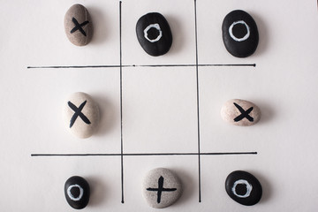 top view of tic tac toe game with stones marked with naughts and crosses on white paper