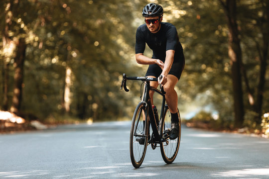 Professional bearded cyclist in sport clothing and protective helmet training with bike on nature.  Disciplined sportsman doing regular activity on fresh air.