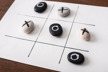 tic tac toe game on white paper with pebbles marked with naughts and crosses on wooden surface