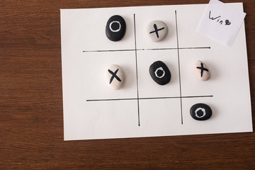 top view of tic tac toe game with stones marked with naughts and crosses, and card with win inscription on wooden surface