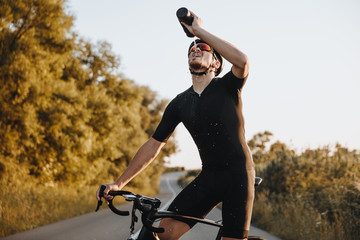 Tired mature man in sport clothing, protective helmet and mirrored glasses drinking fresh water...