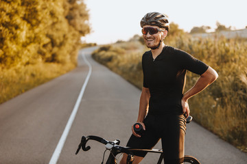 Cheerful bearded man in activewear, black helmet and sport glasses sitting on bike and looking on...