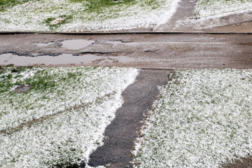 Snow on green grass and puddle on road