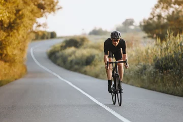Foto op Canvas Professional male cyclist in black helmet, protective glasses and activewear dynamically riding bicycle on paved road with blur background. Concept of summer activity and healthy lifestyle © Tymoshchuk