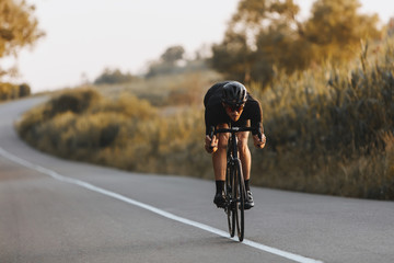 Professional sporty cyclist in black helmet, protective glasses and active wear dynamically riding...