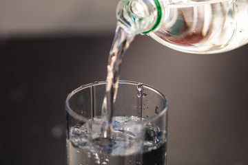 Pouring water from plastic bottle into a glass on blurred background. Selective focus and copy space