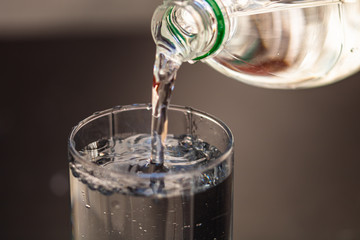 Pouring water from plastic bottle into a glass on blurred background. Selective focus and copy space