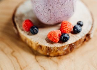 Healthy vitamin shake with dragon fruit, berries, chia seeds and almond milk in a stylish glass, decorated with raspberry and blueberry on a wooden plate, pink, red, bright