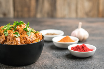 .Chicken tikka masala traditional Asian spicy meat food with rice tomatoes and cilantro in a black bowl on dark background.
