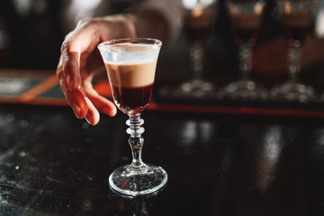 hand takes a layered cocktail at the bar. close-up