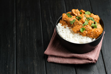 Chicken tikka masala traditional Asian spicy meat food with rice tomatoes and cilantro in a black bowl on dark background.