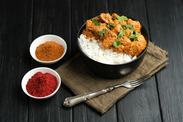 Chicken tikka masala traditional Asian spicy meat food with rice tomatoes and cilantro in a black bowl on dark background.