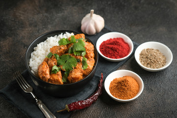 Chicken tikka masala traditional Asian spicy meat food with rice tomatoes and cilantro in a black bowl on dark background.