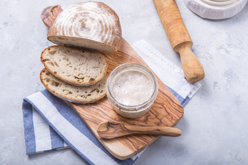 Fresh homemade bubbly sourdough starter, a fermented mixture of water and flour to use as leaven for bread baking, on wooden table