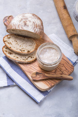 Fresh homemade bubbly sourdough starter, a fermented mixture of water and flour to use as leaven for bread baking, on wooden table