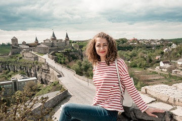 Fototapeta na wymiar Cute curly girl near the old castle in Europe. Top view on road to Castle in Background. Travel and tourism