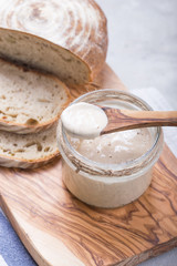 Fresh homemade bubbly sourdough starter, a fermented mixture of water and flour to use as leaven for bread baking, on wooden table