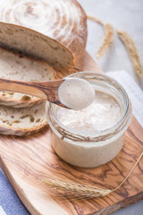 Fresh homemade bubbly sourdough starter, a fermented mixture of water and flour to use as leaven for bread baking, on wooden table
