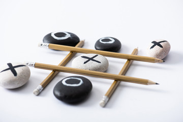 tic tac toe game with grid made of pencils and pebbles marked with naughts and crosses on white surface