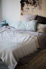 calm gentle bedroom interior. large bed with lots of rugs of pillows and bedspreads. nearby stands a round stool wrapped in blue fabric. On the stool is a vintage radio.