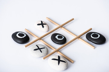 tic tac toe game with grid made of paper tubes, and pebbles marked with naughts and crosses on white surface