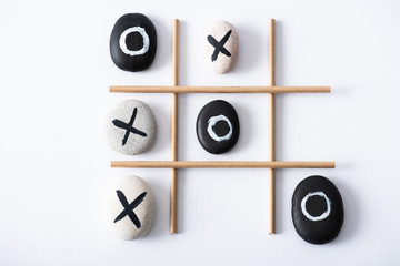 top view of tic tac toe game with grid made of paper tubes, and pebbles marked with naughts and...
