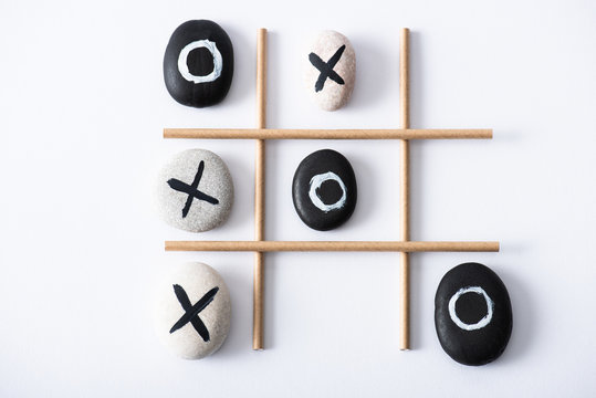 top view of tic tac toe game with grid made of paper tubes, and pebbles marked with naughts and crosses on white surface