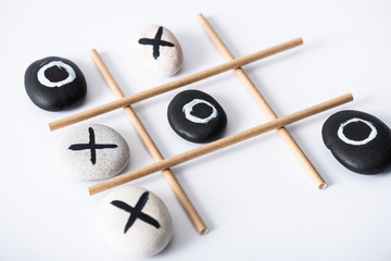 tic tac toe game with grid made of paper tubes, and pebbles marked with naughts and crosses on white surface