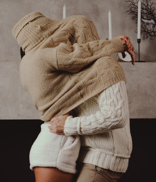 a couple in love in cozy sweaters in warm shades hid together under a sweater hugging.