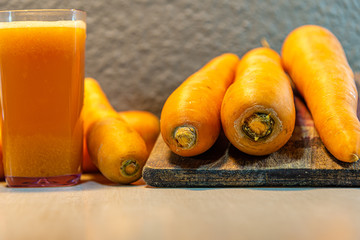 Carrot juice and tubercles (Daucus carota) on light concrete background