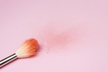 Makeup brush next to the texture of scattered colored face powder. A brush made of goat hair lies against the background of a broken blush