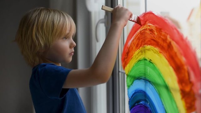 Little boy drawing rainbow on window while coronavirus quarantine. Rainbow sign is symbol of hope, means that everything will be OK. Stay at home for lockdown coronavirus.