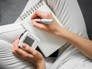 Close-up patient writing notes with blood pressure monitor