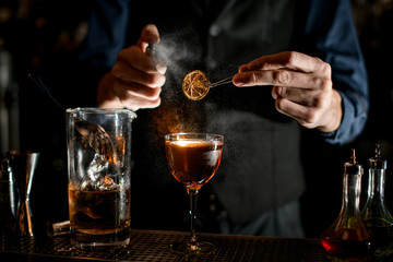 bartender holds tweezers with slice of citrus over glass and sprinkles on it.