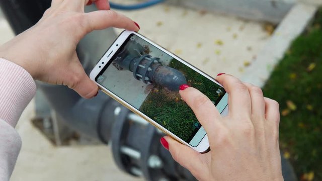 Female engineer photographs with a smartphone water pipes. Quality control and repair concept.