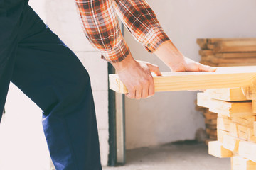 The worker is taking the wooden plank from the pile of lumber
