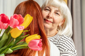 Mother and young daughter are hugging. Happy mother's day. Daughter congratulates mother and gives a bouquet of tulips flowers