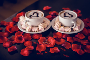 two cups of coffee with steam and rose petals, rings