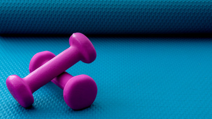 Get fit and lose weight through exercising,physical wellbeing and build muscle with resistance training concept with vivid purple dumbbell isolated on vibrant blue yoga mat background with copy space