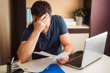 The shocked and disappointed man saw the bad news in the invoices. Frustrated unemployed man with...