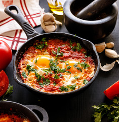 Shakshuka a traditional dish of tomato, eggs and peppers with the addition of aromatic spices and fresh parsley in a cast iron skillet, close up