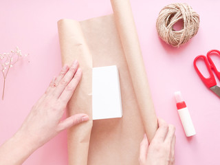 Obraz na płótnie Canvas Step 3. Wrap the box in packaging. DIY tutorial gift wrapping in eco rustic style on pink background. Woman work with package. Сoncept decorating gift with nature materials, do it yourself. Top view