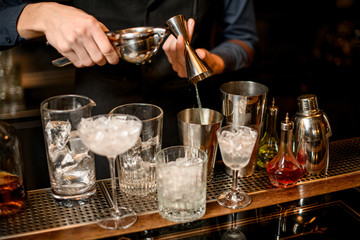 bartender carefully pours squeezed juice from jigger into shaker