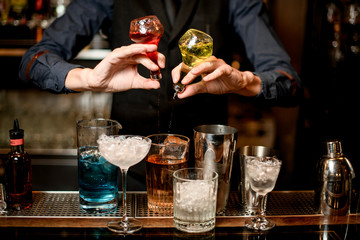 bartender holds bottles with liquor and adds it to glass with cocktail