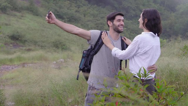 Happy young couple backpack to travel taking a picture with smart mobile phone on mountain, man and woman journey and selfie with smartphone in vacation for leisure, honeymoon and romantic.